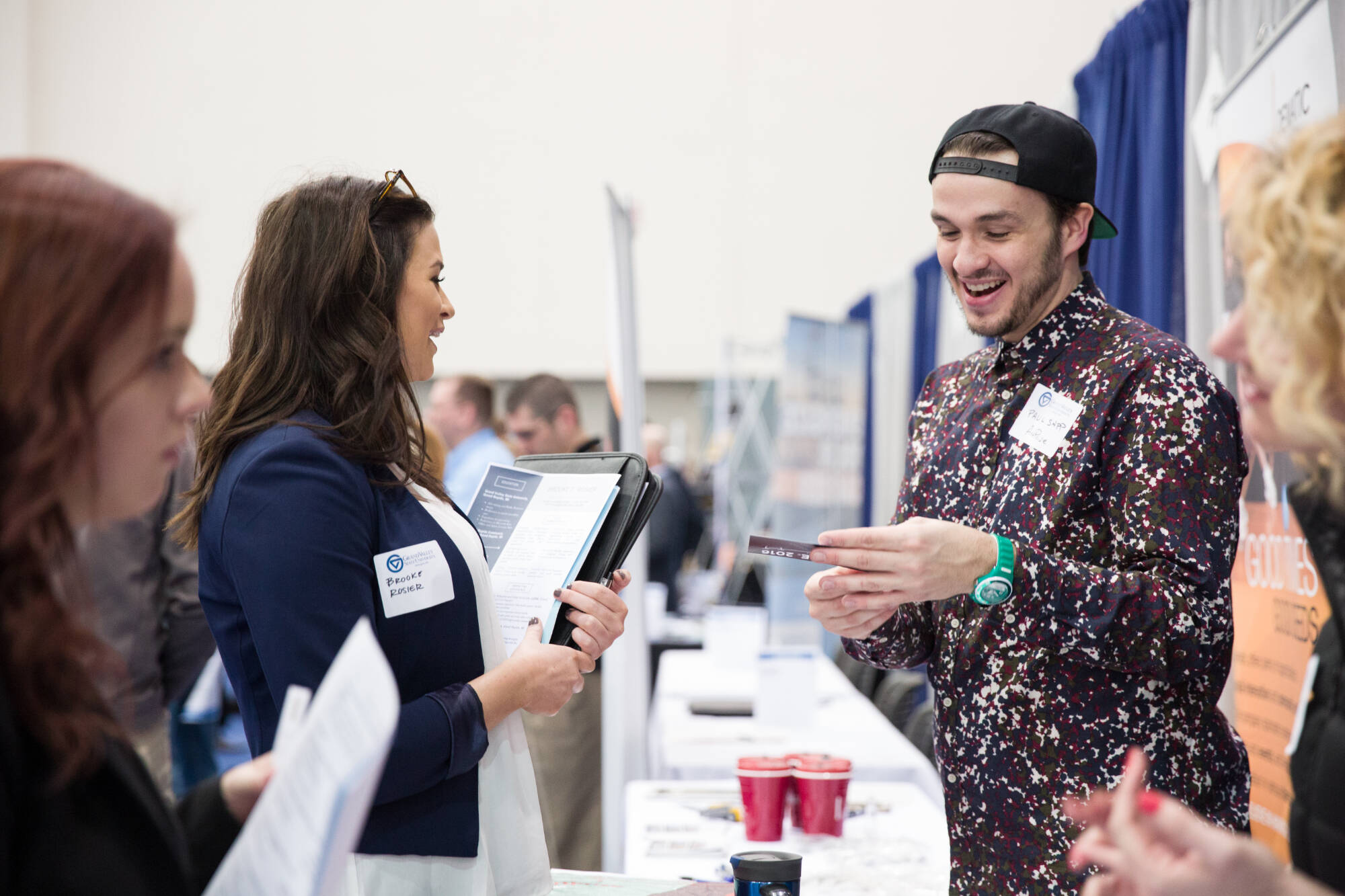 Students and employers engage in conversation at a career fair, exchanging resumes and information at a booth.